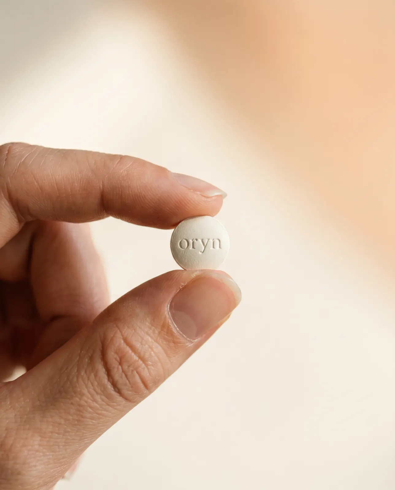 A single Oryn pill held between fingertips